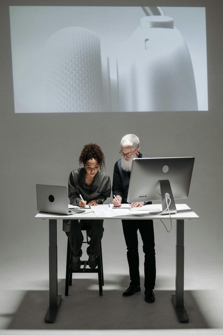 Two professionals collaborate in a high-tech setting with laptops and digital screens.